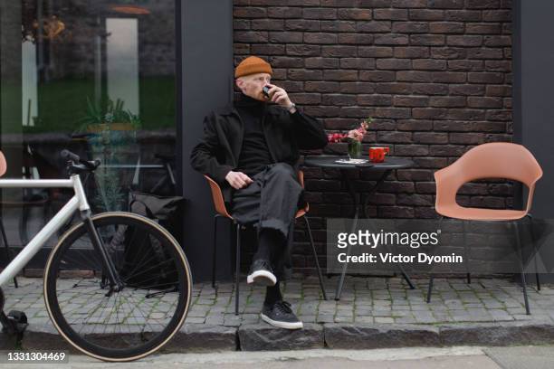 young stylish man enjoys his coffee on the sidewalk - street style man fotografías e imágenes de stock