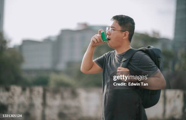 asian chinese mid adult man using asthma inhaler outdoor during sunset carrying back-beg - cystic fibrosis 個照片及圖片檔