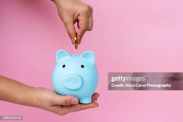 woman hand inserting coin into piggy bank - piggy bank stock-fotos und bilder