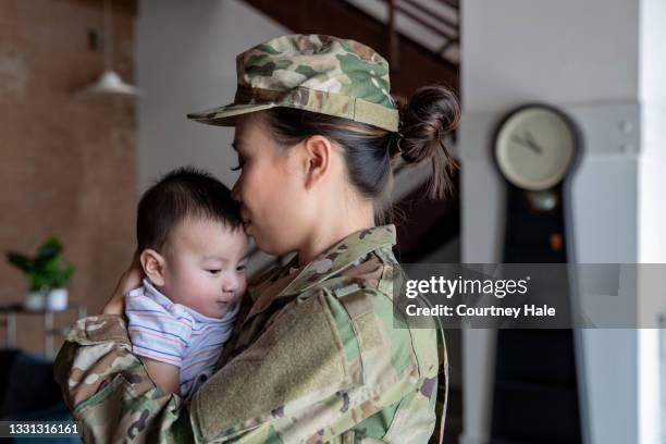 若い女性兵士は、軍事任務を報告する前に、生まれたばかりの息子との絆の瞬間を持っています - asian flags ストックフォトと画像