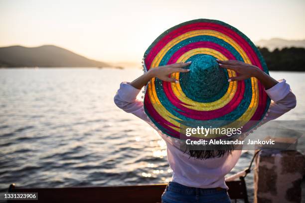 une jeune femme avec un grand sombrero coloré regardant le coucher du soleil au bord de la mer - chapeau mexicain photos et images de collection