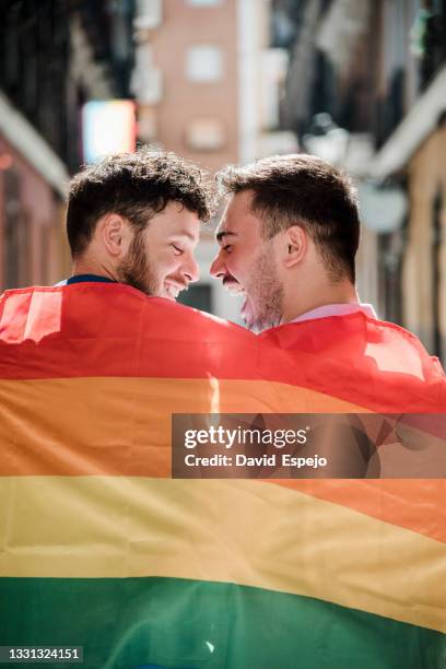 smiling homosexual couple wrapped in lgbt flag - marriage equality stock-fotos und bilder