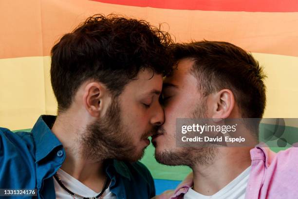 homosexual couple kissing tenderly against rainbow flag - seksediscriminatie stockfoto's en -beelden