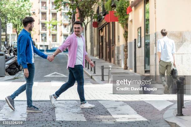 positive gay couple crossing road on zebra - union gay stockfoto's en -beelden