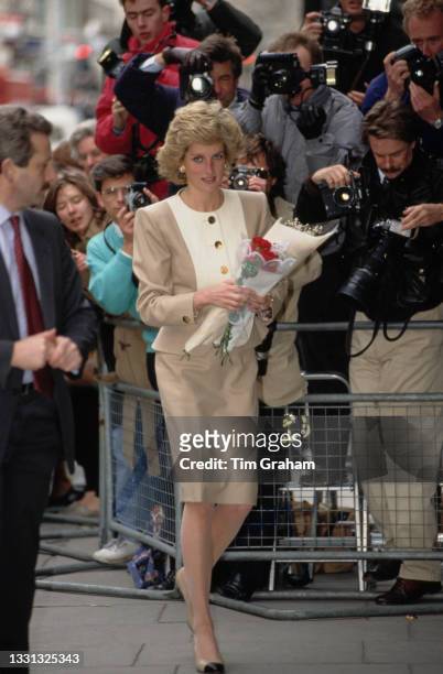 British Royal Diana, Princess of Wales , wearing a beige-and-white suit by Catherine Walker, carrying flowers as she passes a pen of photographers...