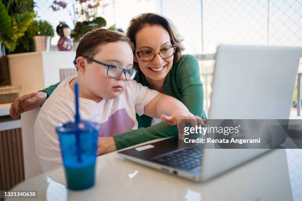 mother helping son with down syndrome in homeschooling. distance learning concept. - special needs children stock pictures, royalty-free photos & images