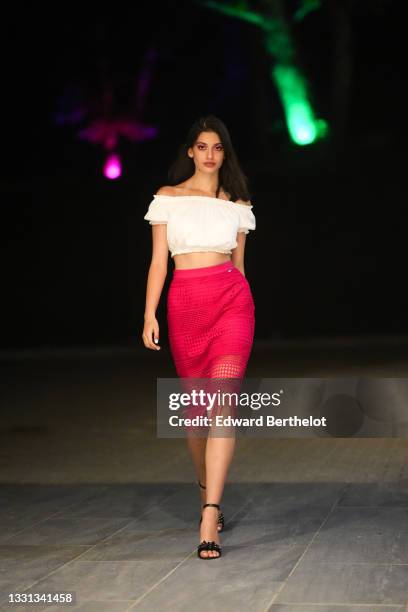 Model Irina Motoc wears a white off-shoulder ruffled and gathered cropped top, a knee length red skirt with fringes and patterns, black high heeled...