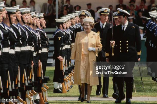 British Royal Queen Elizabeth II, wearing an orange coat and a white hat with an orange gingham decorative detail and a veil, during an inspection as...
