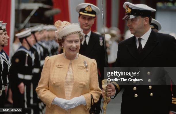 British Royal Queen Elizabeth II, wearing an orange coat and a white hat with an orange gingham decorative detail and a veil, during an inspection as...