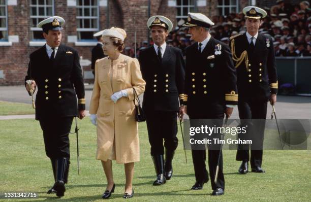 British Royal Queen Elizabeth II, wearing an orange coat and a white hat with an orange gingham decorative detail and a veil, attends a...