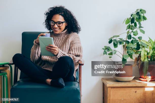 cheerful woman drinking coffee and using a digital tablet - armstoel stockfoto's en -beelden