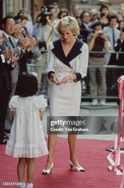 British Royal Diana, Princess of Wales , wearing a white outfit with a black collar, lapels and cuffs, with a young Japanese girl attends the opening...