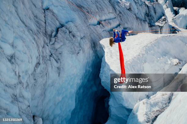 a women performs dynamic tricks from an aerial hammock deep with in a glacier crevasse - yoga in the snow stock-fotos und bilder