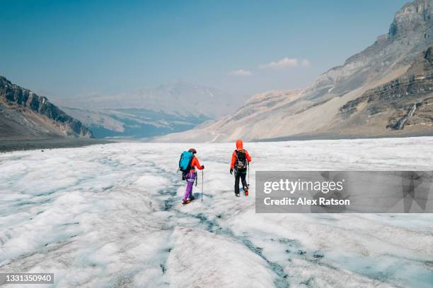 two female mountaineers walks down the ice of the athabasca glacier - columbia icefield stock pictures, royalty-free photos & images