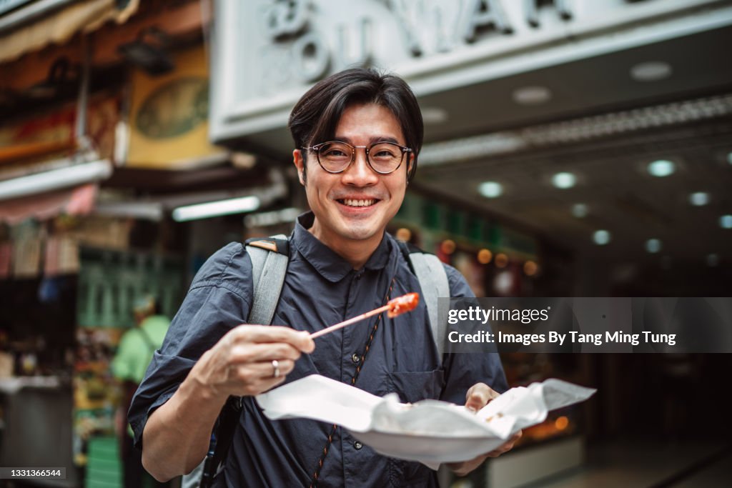 Young handsome man enjoying Hong Kong local street food joyfully in street