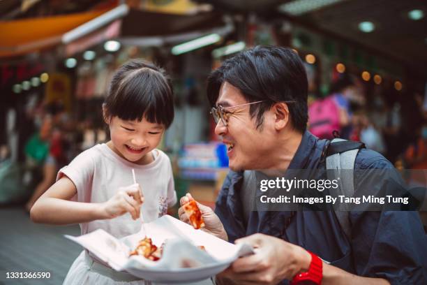 dad & daughter enjoying hong kong local street food joyfully in street - un giorno nella vita foto e immagini stock