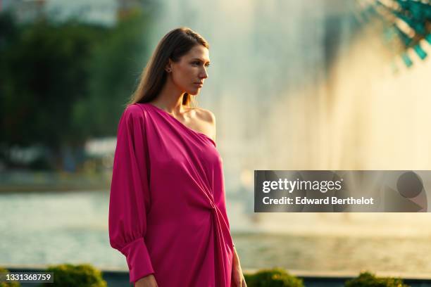 Landiana Cerciu wears a one-shoulder neon pink silky lustrous midi dress with a puff sleeve, on July 27, 2021 in Sibiu, Romania.