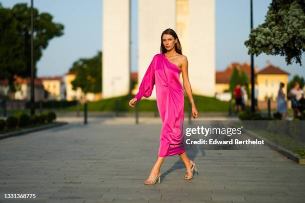 Landiana Cerciu wears a one-shoulder neon pink silky lustrous midi dress with a puff sleeve, on July 27, 2021 in Sibiu, Romania.