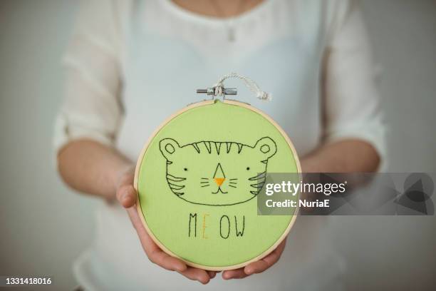 woman holding an embroidery hoop with a cat's face and the word meow - embroidery frame stock pictures, royalty-free photos & images