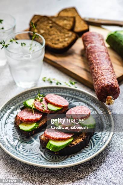 slices of salami, cucumber and rye bread on a chopping board with two glasses of water - rye bread stock pictures, royalty-free photos & images