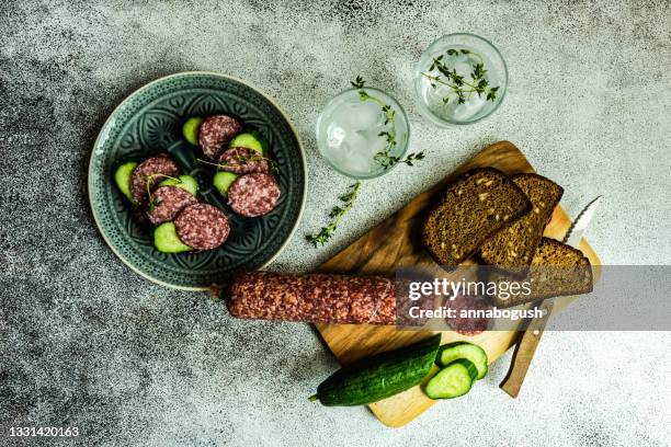 slices of salami, cucumber and rye bread on a  chopping board with two glasses of water - brotzeitbrett stock-fotos und bilder