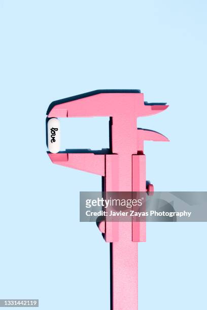 pink vernier gauge calliper measuring love pill on blue background - mass unit of measurement stock-fotos und bilder