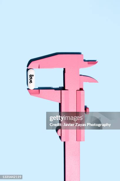 pink vernier gauge calliper measuring love pill on blue background - meter instrument of measurement stock pictures, royalty-free photos & images