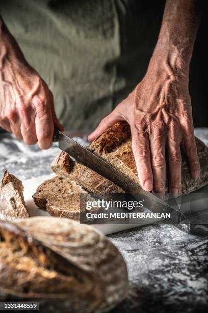 male hands cutting sourdough bread slices wholegrain homemade german style on cutting board - rye bread stock pictures, royalty-free photos & images