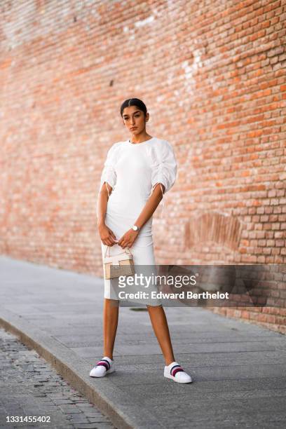 Jacqueline Barth wears a white midi dress with ruffled / gathered puff shoulders, a beige wicker bag, Tommy Hilfiger sneakers shoes, on July 27, 2021...