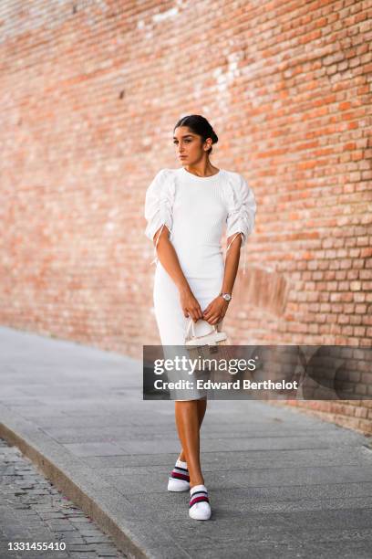 Jacqueline Barth wears a white midi dress with ruffled / gathered puff shoulders, a beige wicker bag, Tommy Hilfiger sneakers shoes, on July 27, 2021...