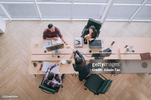 directly above high angle view Asian colleague with Indian coworker in wheelchair taking a break eating sharing bread snack at their office workstation