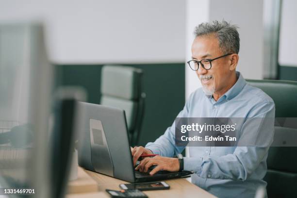 hombre mayor chino asiático con vello facial usando la escritura de la computadora portátil que trabaja en el plan abierto de la oficina - small office fotografías e imágenes de stock