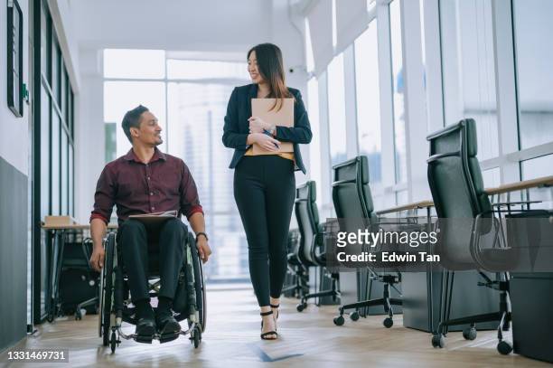 indian white collar male worker in wheelchair having cheerful discussion conversation with his female asain chinese colleague coworking at walkway corridor - werkplek stockfoto's en -beelden