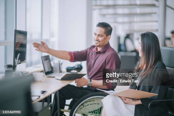 indian white collar male worker in wheelchair having cheerful discussion conversation with his female asain chinese colleague coworking in creative office workstation beside window - disabled accessibility stock pictures, royalty-free photos & images
