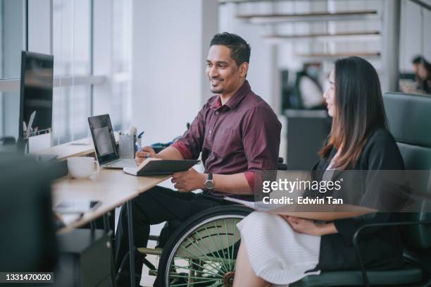 indian white collar male worker in wheelchair having cheerful discussion conversation with his female asain chinese colleague coworking in creative office workstation beside window - disabled accessibility stock pictures, royalty-free photos & images