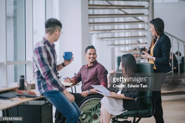 indian white collar male worker in wheelchair having cheerful discussion leading conversation with colleague in creative office workstation beside window - beroep stockfoto's en -beelden