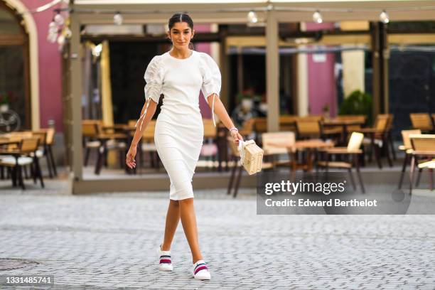 Jacqueline Barth wears a white midi ribbed dress with ruffled / gathered puff shoulders, a beige wicker bag, Tommy Hilfiger sneakers shoes, on July...