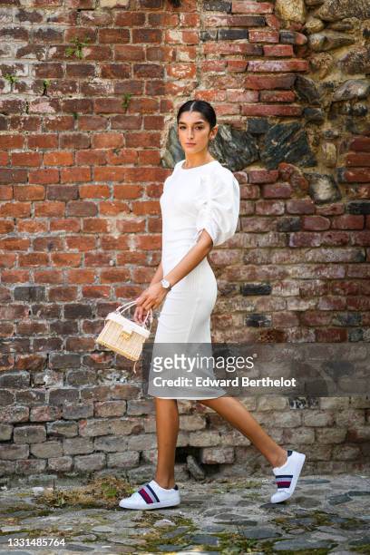 Jacqueline Barth wears a white midi ribbed dress with ruffled / gathered puff shoulders, a beige wicker bag, Tommy Hilfiger sneakers shoes, on July...
