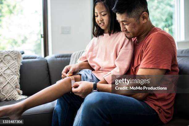 father putting band-aid on daughter - knees together - fotografias e filmes do acervo