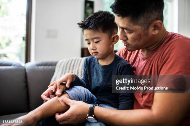 father putting band-aid on son - applying bandage stock pictures, royalty-free photos & images