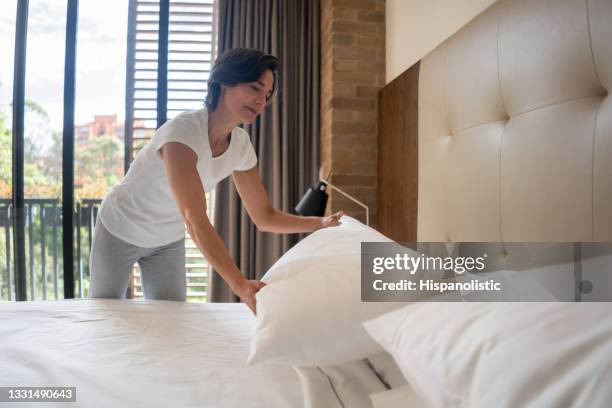 woman at home making the bed and arranging the pillows - travesseiro imagens e fotografias de stock