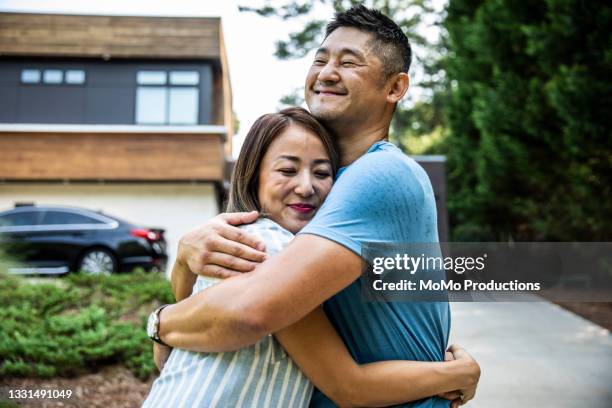 husband and wife embracing in front of modern home - best before stockfoto's en -beelden