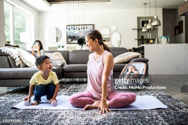 mother doing yoga at home surrounded by children - family yoga photos et images de collection