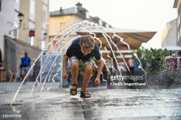 little boy running through the public fountain on a street.  design: arch. di eduard widmann und arch. mag. erich wagner - salzburg 個照片及圖片檔