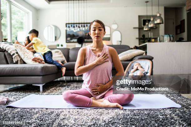 mother doing yoga at home surrounded by children - yoga rug stock pictures, royalty-free photos & images