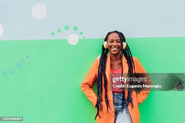 italy, milan, portrait of stylish woman with headphones against wall - multi colored coat stock pictures, royalty-free photos & images