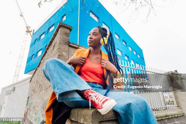 italy, milan, portrait of woman in orange coat against rusty metal fence - orange shoe foto e immagini stock