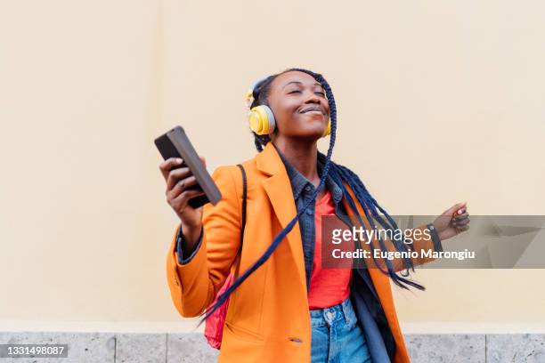 italy, milan, woman with headphones and smart phone dancing outdoors - luisteren stockfoto's en -beelden