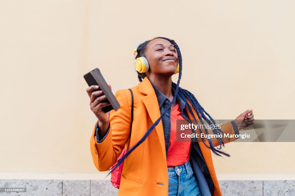 Italy, Milan, Woman with headphones and smart phone dancing outdoors
