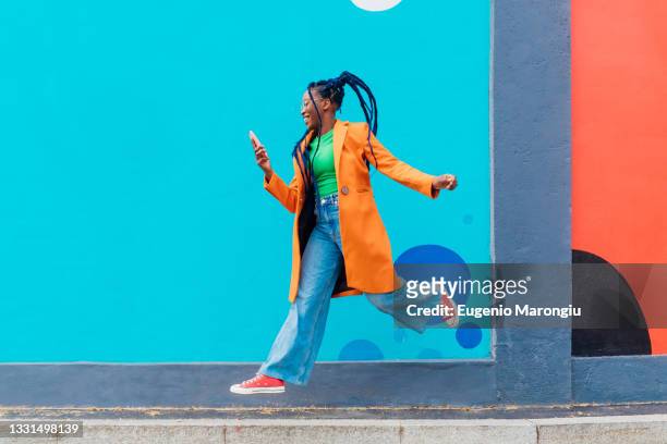 italy, milan, woman with braids jumping against blue wall - fashion stock-fotos und bilder